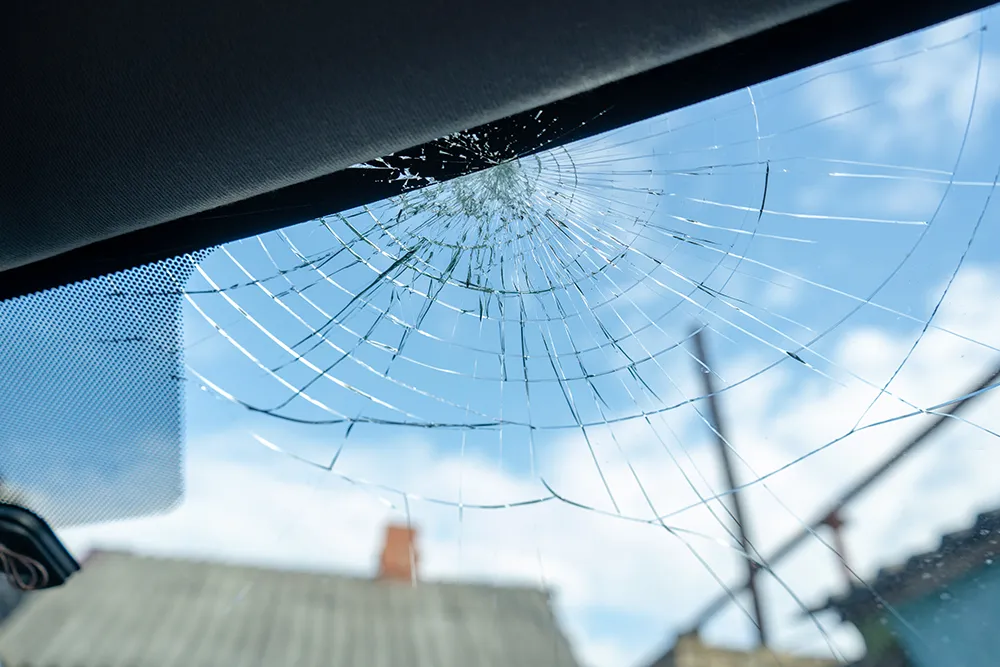 Broken windshield with a lot of cracks and small glass pieces, damaged car
